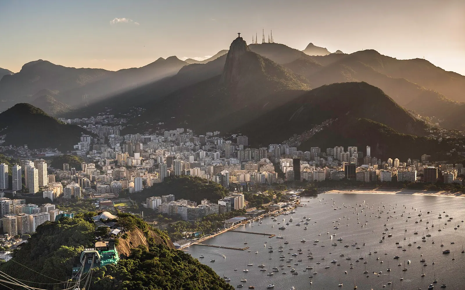 The skyline of the city and the Sugarloaf at sunset, crepuscular rays spreading over the bay. Rio de Janeiro, Brazil.
