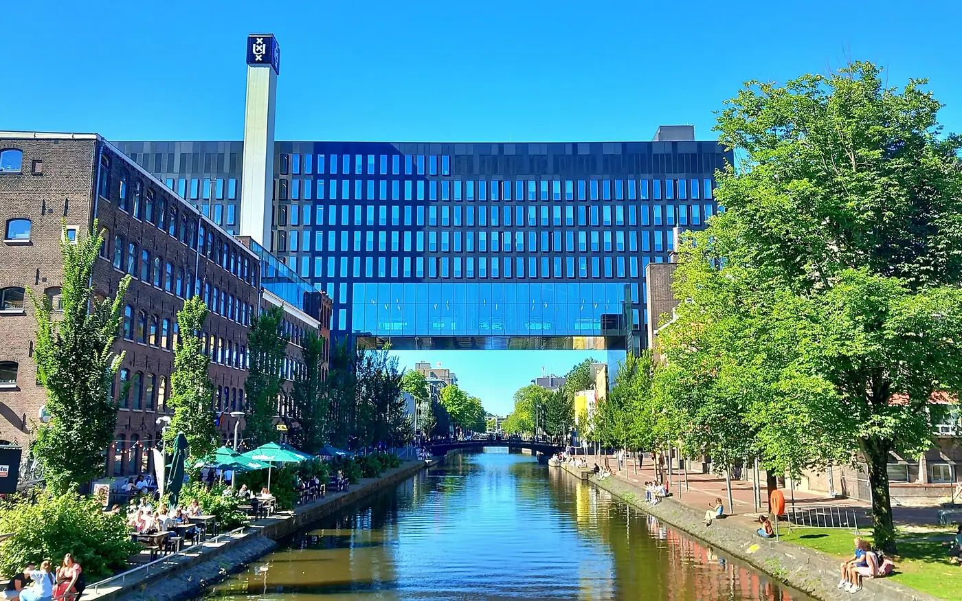 The Roeterseiland campus of the University of Amsterdam in September of 2023, the second day of the academic year, with students sitting next to the canal, viewed from the Theodore Limpergbrug bridge